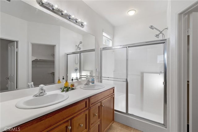 bathroom featuring a walk in closet, double vanity, a stall shower, and a sink