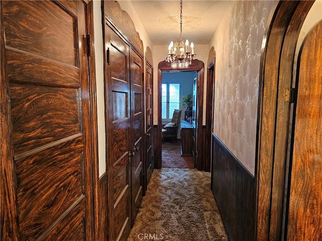 hall with arched walkways, wood walls, dark carpet, and an inviting chandelier