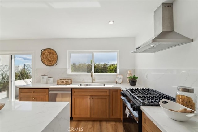 kitchen featuring light wood-style flooring, gas stove, a sink, wall chimney range hood, and dishwasher