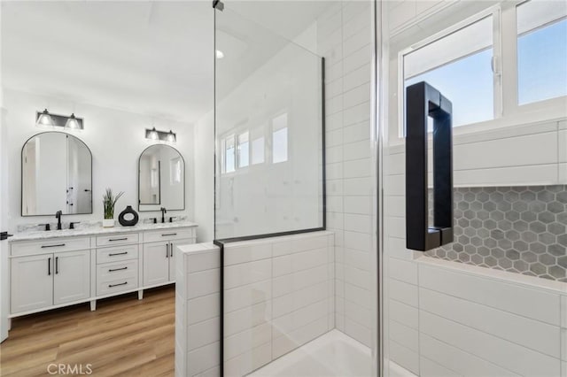 full bath featuring double vanity, a sink, a tile shower, and wood finished floors