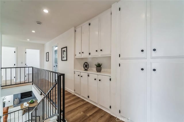 hallway with recessed lighting, wood finished floors, and an upstairs landing