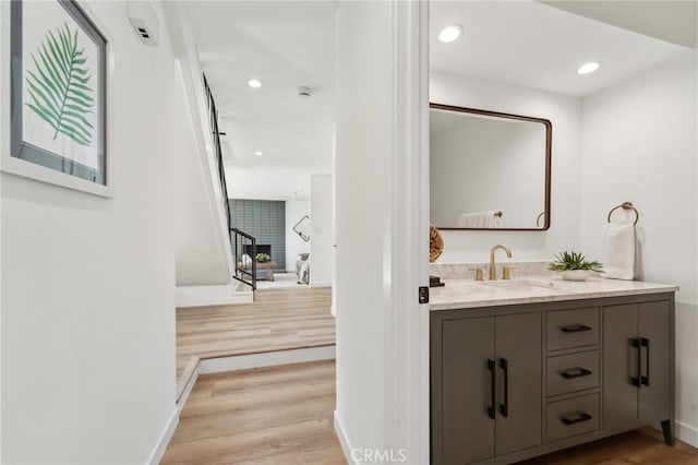 bathroom featuring baseboards, wood finished floors, vanity, and recessed lighting