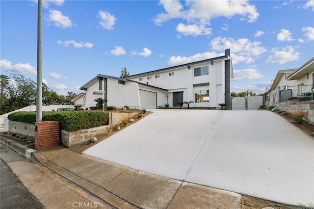 view of front of house with a garage, concrete driveway, fence, and stucco siding