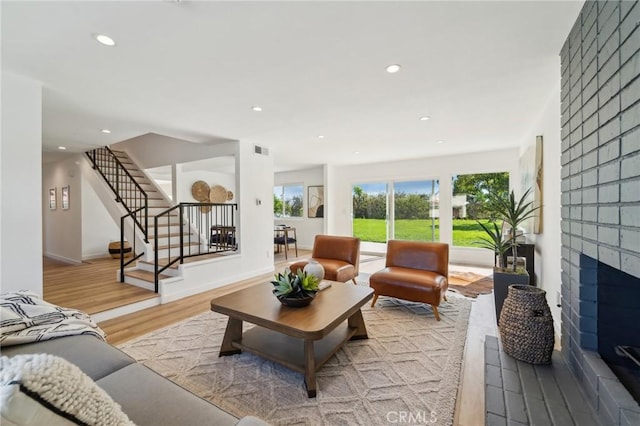 living area with light wood-style flooring, recessed lighting, visible vents, stairs, and a brick fireplace