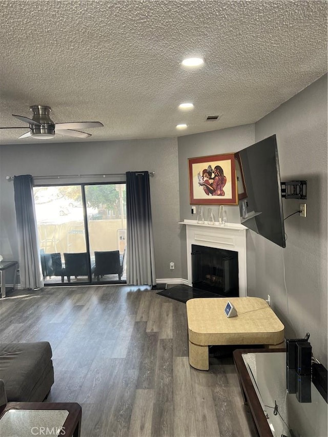 living area featuring ceiling fan, a textured ceiling, wood finished floors, visible vents, and a glass covered fireplace