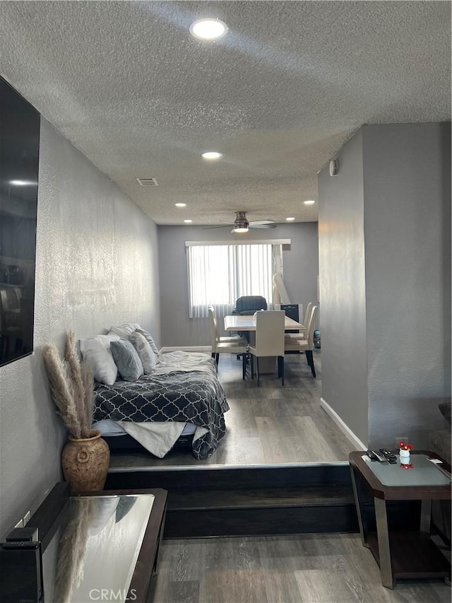 bedroom with a textured ceiling, a textured wall, wood finished floors, visible vents, and baseboards