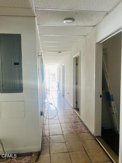 hall with tile patterned flooring, electric panel, and a drop ceiling