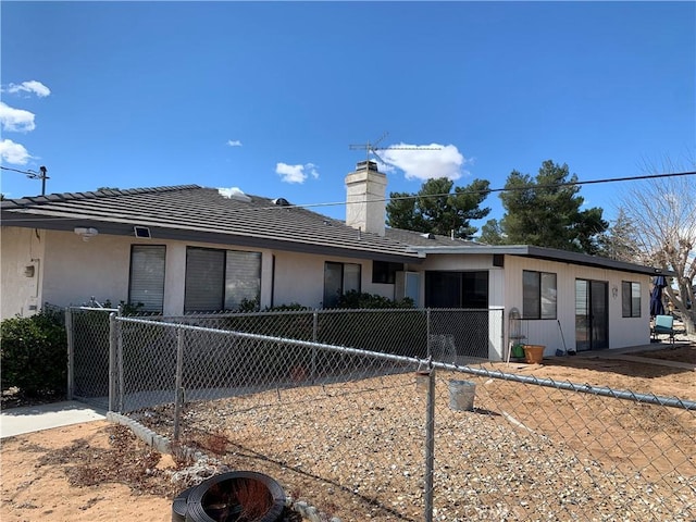 back of house featuring a fenced front yard, a chimney, and stucco siding