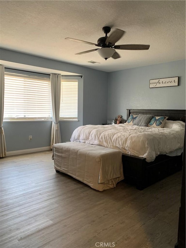 bedroom featuring visible vents, ceiling fan, a textured ceiling, wood finished floors, and baseboards