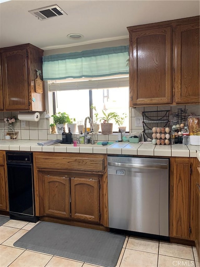 kitchen featuring tasteful backsplash, visible vents, tile counters, dishwasher, and light tile patterned flooring