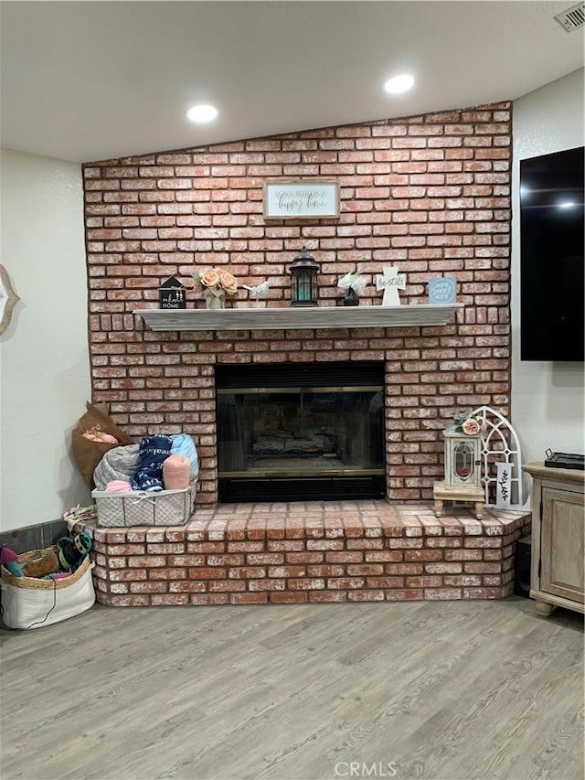 details with a brick fireplace, visible vents, wood finished floors, and recessed lighting