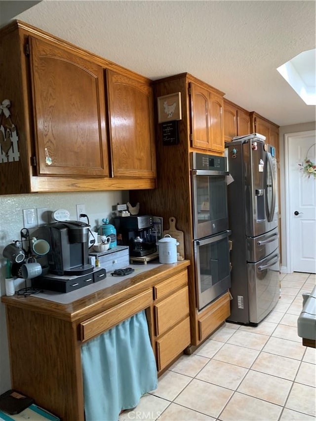 kitchen with a skylight, light tile patterned floors, brown cabinets, stainless steel appliances, and a textured ceiling