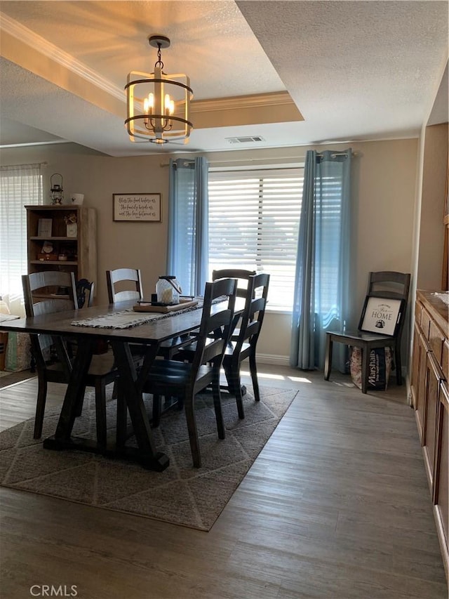 dining room featuring dark wood-style floors, a tray ceiling, visible vents, ornamental molding, and a textured ceiling