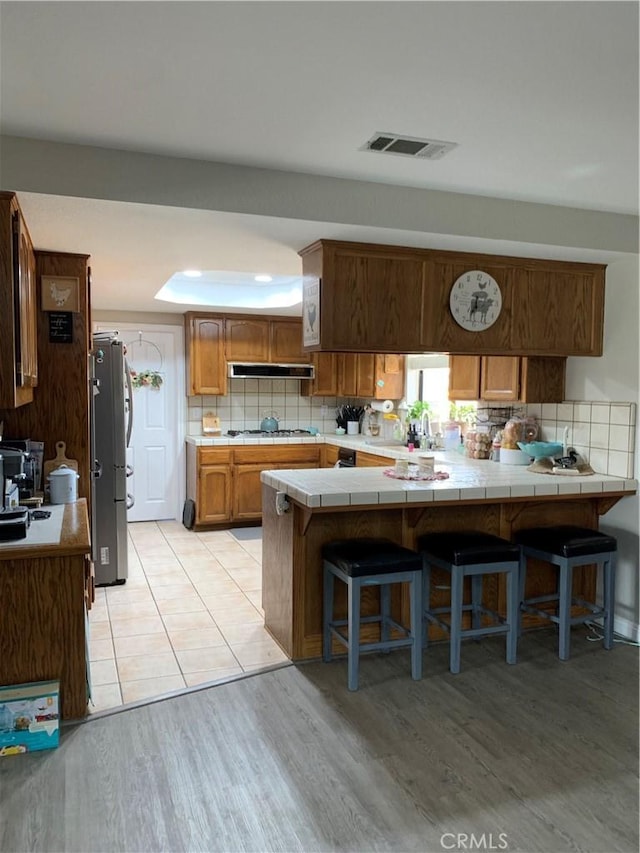 kitchen featuring tile countertops, visible vents, decorative backsplash, freestanding refrigerator, and a peninsula