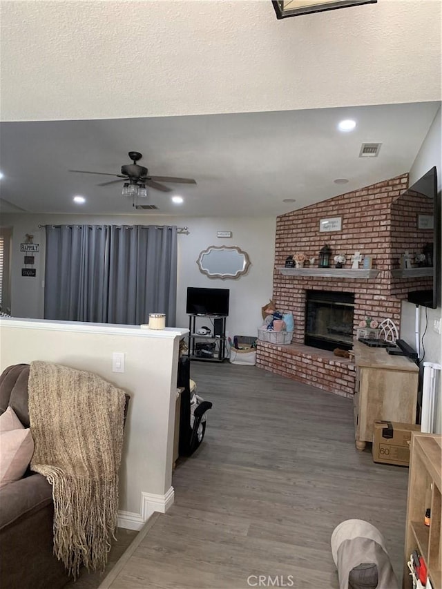 living area featuring recessed lighting, wood finished floors, visible vents, a ceiling fan, and a brick fireplace