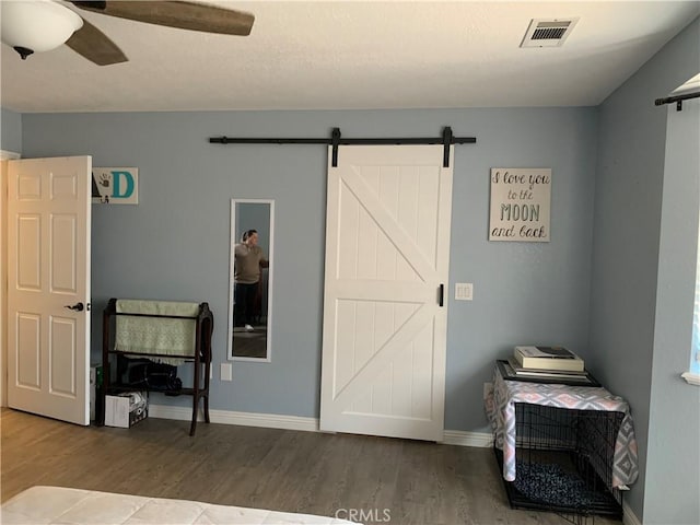 bedroom with a barn door, wood finished floors, visible vents, and baseboards