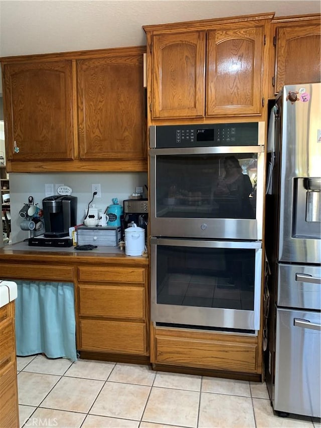 kitchen with brown cabinetry, light tile patterned floors, and stainless steel appliances