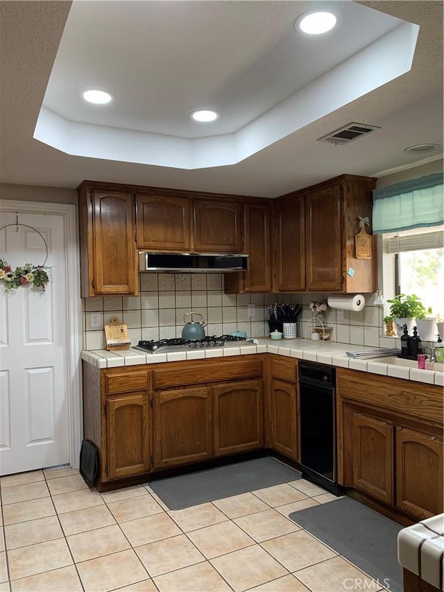 kitchen featuring under cabinet range hood, visible vents, stainless steel gas cooktop, and a raised ceiling