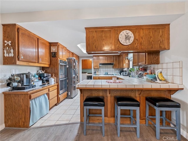 20312 Eyota Rd, Apple Valley, CA 92308 - kitchen with a peninsula, stainless steel appliances, tile counters, under cabinet range hood, and washer and dryer