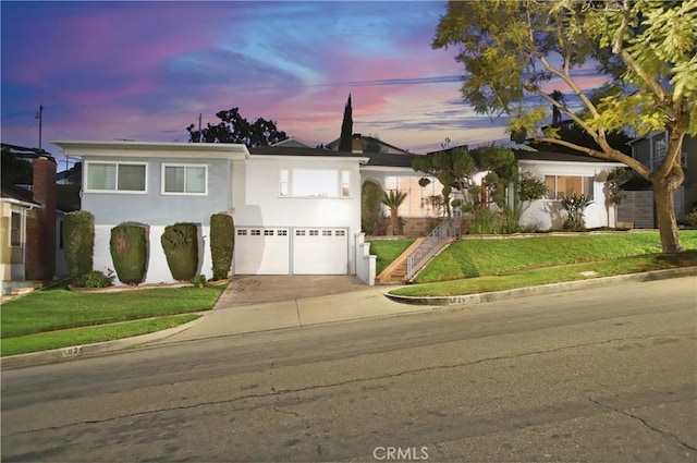 view of front of home with driveway, an attached garage, stucco siding, stairs, and a lawn