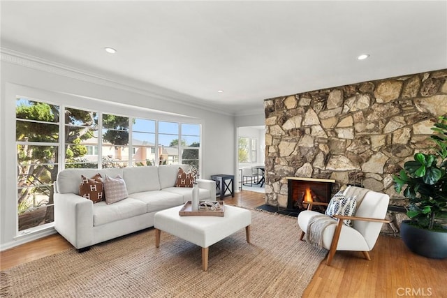 living room featuring a stone fireplace, recessed lighting, wood finished floors, and ornamental molding