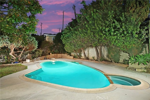 pool at dusk featuring a fenced backyard and a pool with connected hot tub