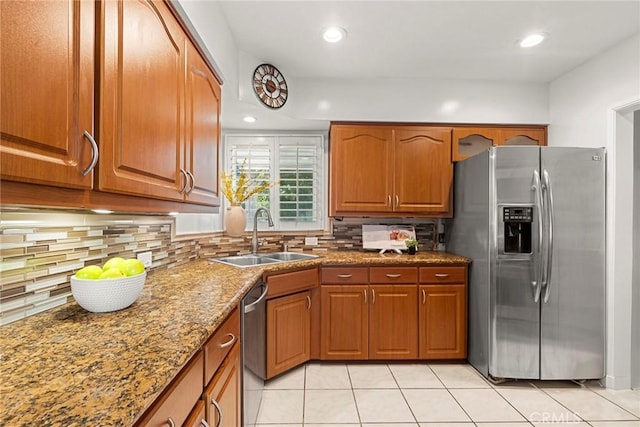 kitchen featuring light tile patterned floors, brown cabinetry, a sink, decorative backsplash, and stainless steel appliances