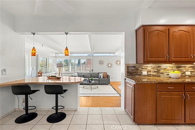 kitchen featuring dark stone countertops, a kitchen bar, tasteful backsplash, and brown cabinetry