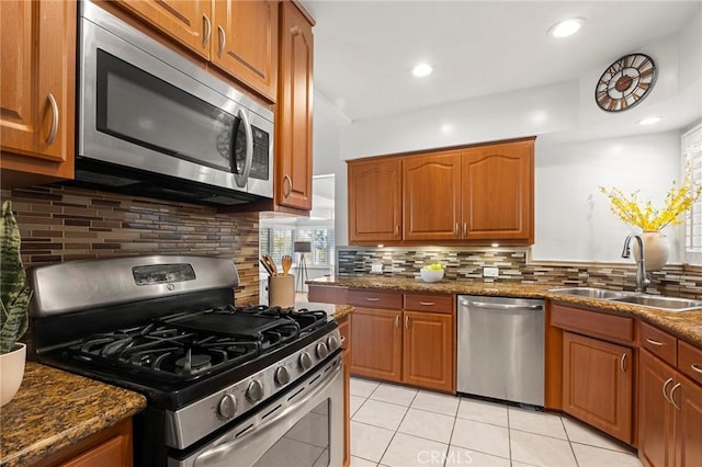 kitchen with dark stone countertops, brown cabinets, stainless steel appliances, and a sink