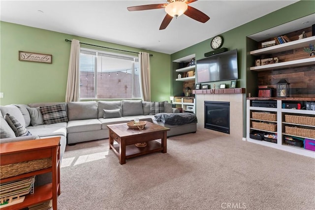 carpeted living room with built in features, ceiling fan, and a tiled fireplace