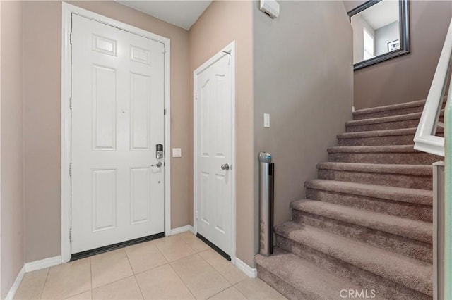 foyer entrance with light tile patterned floors, stairs, and baseboards