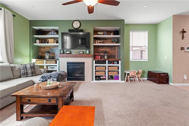 living area with baseboards, built in features, a ceiling fan, a tiled fireplace, and carpet