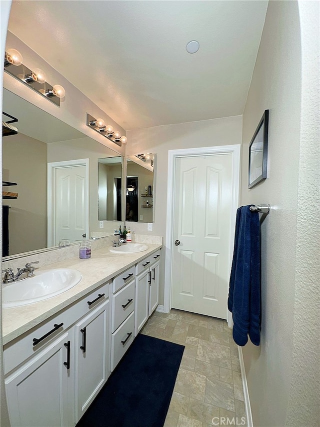 bathroom featuring baseboards, double vanity, and stone finish floors