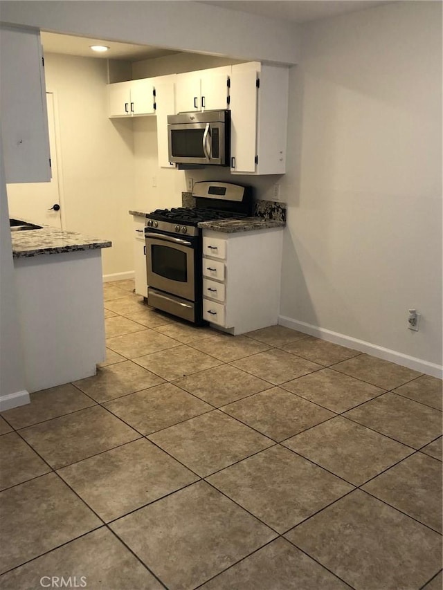 kitchen with light tile patterned floors, white cabinetry, baseboards, appliances with stainless steel finishes, and dark stone counters