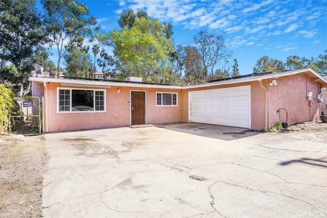 single story home with a garage, fence, driveway, roof mounted solar panels, and stucco siding