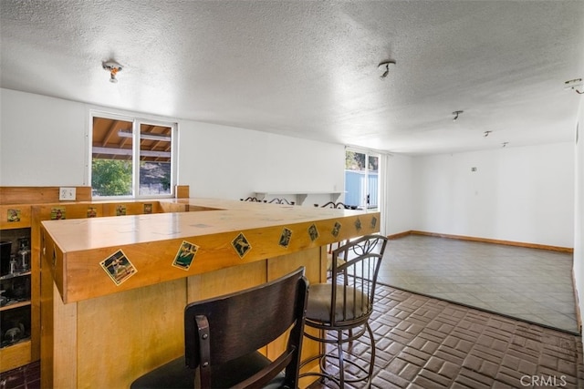 kitchen with open floor plan, a textured ceiling, brick floor, and baseboards