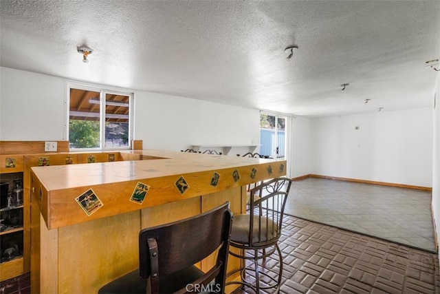 kitchen with brick floor, baseboards, open floor plan, and a textured ceiling