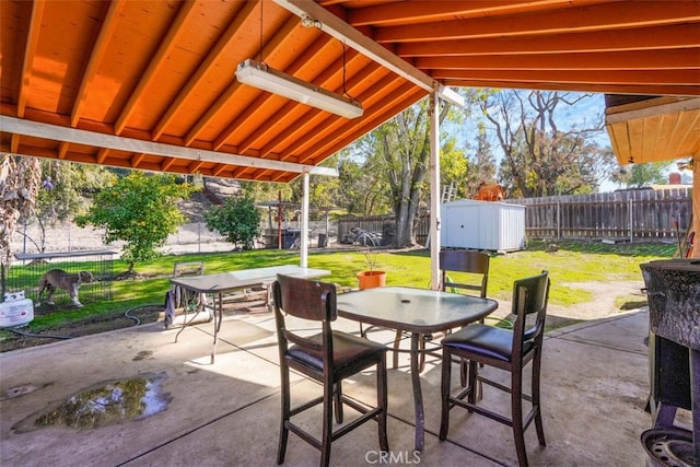 view of patio with outdoor dining space, a fenced backyard, an outbuilding, and a storage unit