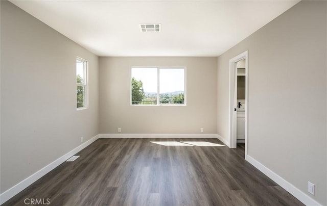 unfurnished room with baseboards, visible vents, and dark wood finished floors