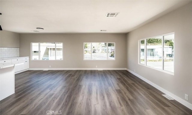 unfurnished living room with baseboards, visible vents, and dark wood-type flooring