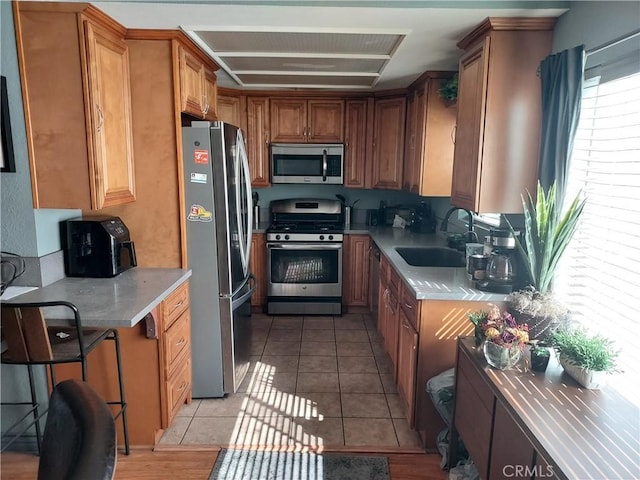 kitchen featuring brown cabinets, light tile patterned floors, stainless steel appliances, light countertops, and a sink