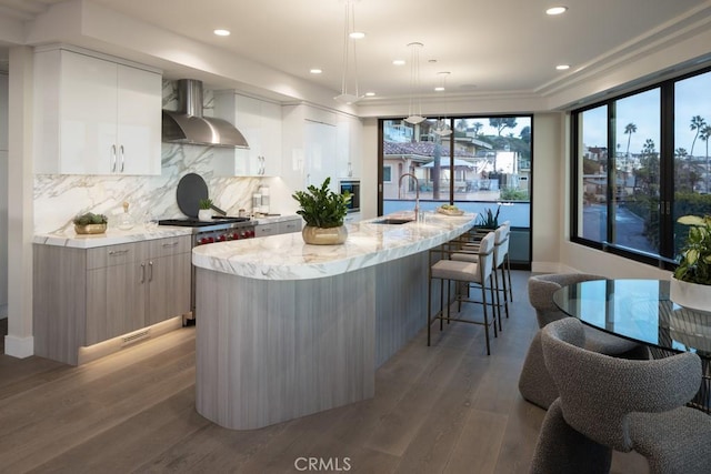 kitchen featuring light wood-style floors, an island with sink, modern cabinets, wall chimney range hood, and a sink