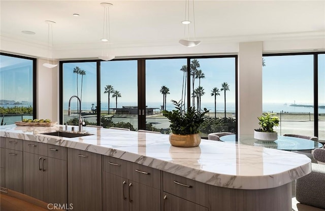 kitchen with a water view, light stone countertops, hanging light fixtures, dark brown cabinets, and a sink