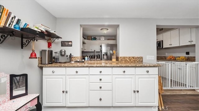 kitchen featuring light stone counters, appliances with stainless steel finishes, white cabinets, a sink, and wood finished floors