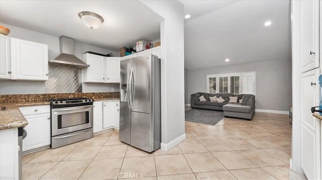 kitchen with wall chimney range hood, white cabinetry, light tile patterned floors, and appliances with stainless steel finishes