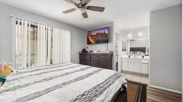 bedroom with a textured ceiling, ensuite bathroom, wood finished floors, a ceiling fan, and baseboards