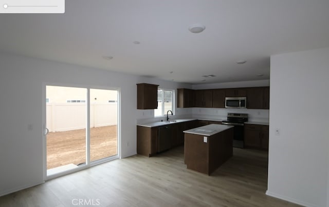 kitchen with a center island, stainless steel appliances, a sink, dark brown cabinets, and light wood-type flooring