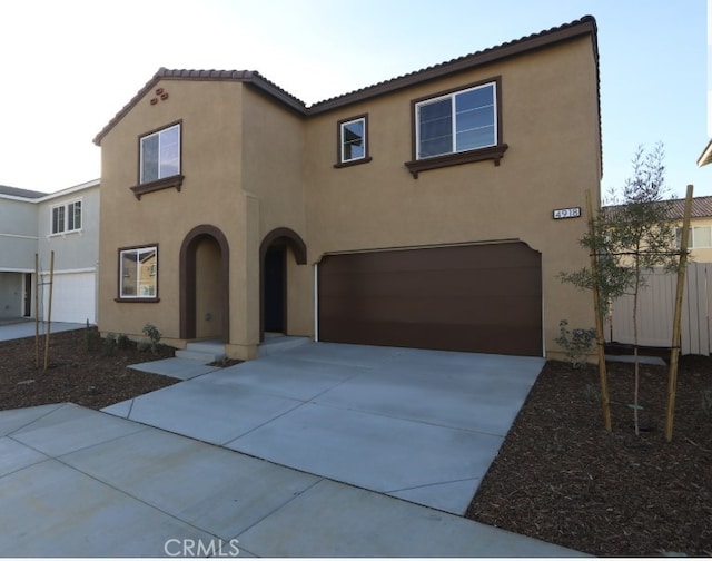 mediterranean / spanish house featuring driveway, an attached garage, a tile roof, and stucco siding