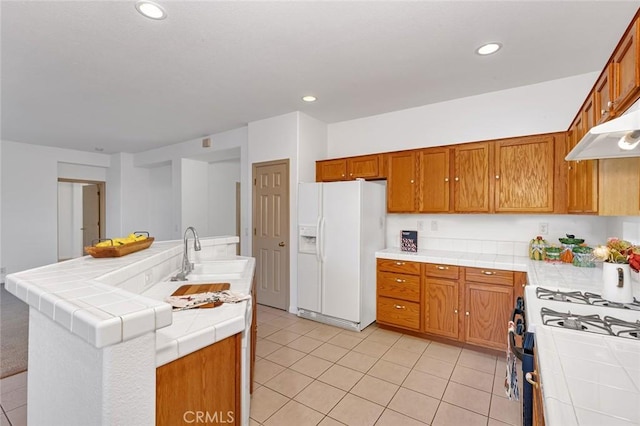 kitchen featuring tile countertops, under cabinet range hood, white fridge with ice dispenser, a sink, and recessed lighting