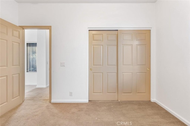 unfurnished bedroom featuring baseboards, a closet, and light colored carpet